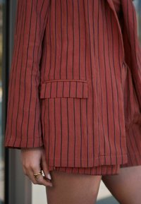 Blazer à rayures rouges avec un joli détail de poche, fabriqué dans un tissu texturé. Manches courtes et shorts assortis visibles. Bague d'accentuation à la main.