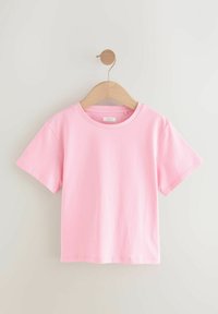 Camiseta de algodón rosa con mangas cortas, cuello redondo, textura suave y detalles de costura. Colgada en un perchero de madera sobre un fondo claro.