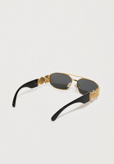 Oválne slnečné okuliare so zlatým kovovým rámom a čiernymi plastovými ramenami. Tmavosivé šošovky; zlaté akcenty s logom na spánku.