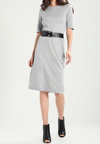 Robe en jersey grise à manches courtes, taille cintrée, ceinture en cuir noir avec boucle ronde, associée à des bottines noires à bout ouvert.