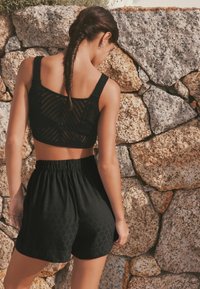 Schwarzes gestricktes Crop-Top mit strukturiertem Muster und breiten Trägern, kombiniert mit lockeren schwarzen Shorts mit einem elastischen Bund und dezentem Design.
