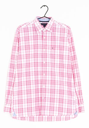 Camisa de manga larga con botones, con patrón de cuadros blancos y rosas, colgada en una percha negra sobre un fondo blanco.