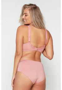 Ensemble de lingerie rose clair comprenant un soutien-gorge avec des bretelles réglables et une fermeture à crochets, associé à une culotte taille haute. Texture lisse.