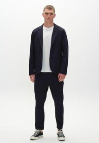 Navy blazer with two chest pockets, paired with a white t-shirt and navy trousers. Black and white sneakers complete the look. Smooth fabric.