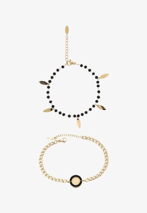 Két aranyszínű karkötő: az egyik fekete gyöngyökkel és öt lógó levél medállal, a másik egy láncszemes karkötő központi fekete-arany medállal.