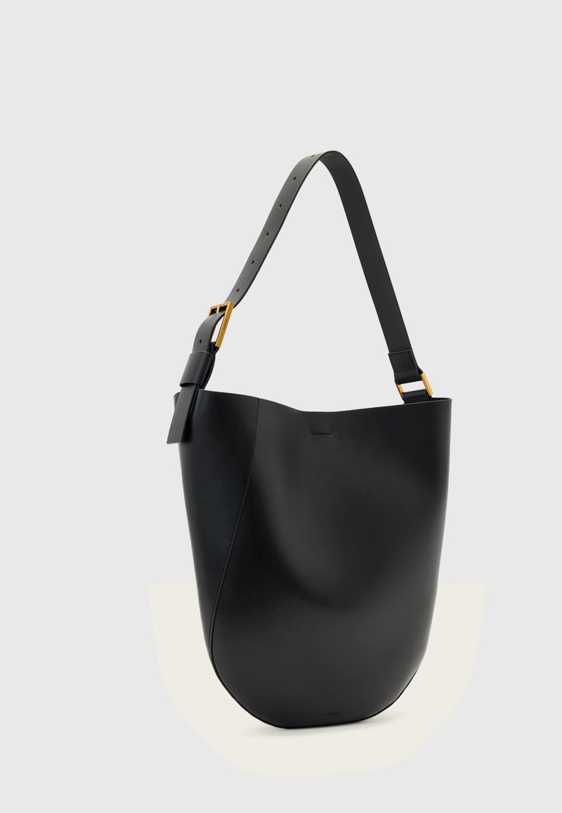Sac seau en cuir noir avec bandoulière réglable et boucle dorée sur un fond uni gris clair.