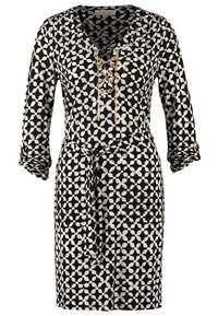 Robe noire et blanche à motifs longueur genou avec manches 3/4, détail lacé doré à l'encolure en V, et ceinture en tissu assorti nouée à la taille.
