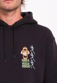 Zwart hoodie met kleurrijke, geborduurde graphics: een bloem en drie skeletfiguren. Tekst luidt "DE BASIS VAN MOLECULAIRE OVERERFING."