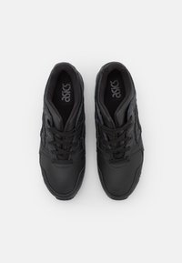 Svarta sportskor med ovandel i texturerat läder, snörning och vadderad krage. Har Asics-logotypen på plösen.