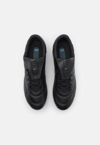 Baskets noires en cuir avec un bout arrondi, un dessus texturé et un col rembourré. Elles présentent des lacets noirs et un logo Nike bleu discret.