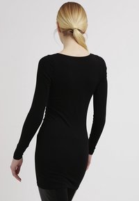 El vestido negro de manga larga presenta un diseño ajustado, tejido suave, escote redondo y se extiende hasta la mitad del muslo, mostrando una textura lisa.