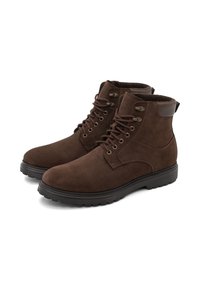 Botas de ante marrón hasta el tobillo con puntera redonda, ojales de metal, cordones robustos y una suela de goma oscura en contraste. Detalle de cuero suave en el tacón.