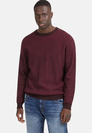 Maglione bordeaux con texture, collo a girocoscia a coste e polsini marrone scuro a contrasto, abbinato a jeans in denim azzurro chiaro.