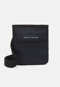 Marineblaue Nylon-Umhängetasche mit verstellbarem schwarzen Tragegurt, Klappe auf der Vorderseite und Logo. Glatte Textur, rechteckige Form, minimalistisches Design.