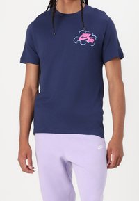 Tmavě modré bavlněné tričko s krátkými rukávy, na hrudi s růžovo-modrým logem "Nike Air". Doplněno světle fialovými tepláky.