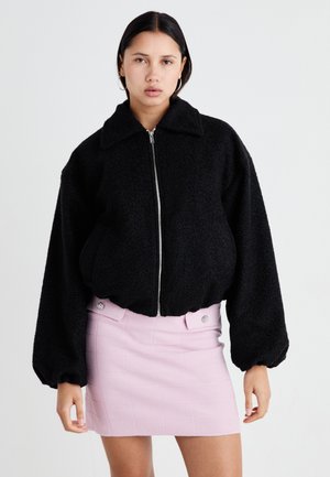Svart fleece bomberjacka med bred krage, dragkedja och voluminösa ärmar, styler med en ljusrosa texturerad kjol med knappar.
