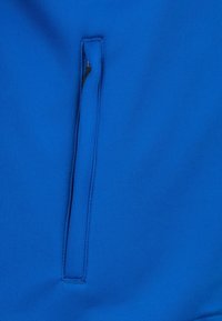 Tessuto blu con una texture liscia, caratterizzato da una tasca con zip verticale sul lato sinistro. Nessun motivo o accentuazione visibile.