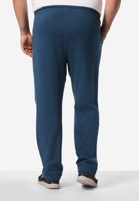 Marineblaue Sweatpants aus weichem Stoff, mit einem elastischen Bund, seitlichen Taschen und schmal zulaufenden Beinen, kombiniert mit dunklen Turnschuhen.