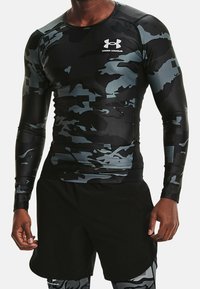 Atleet in zwart en grijs camouflage Under Armour langwerpig compressieshirt met zwarte shorts en bijpassende leggings.