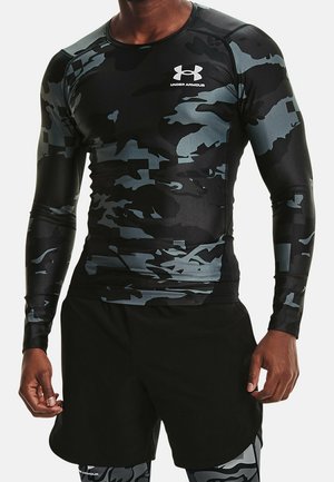 Atleet in zwart en grijs camouflage Under Armour langwerpig compressieshirt met zwarte shorts en bijpassende leggings.