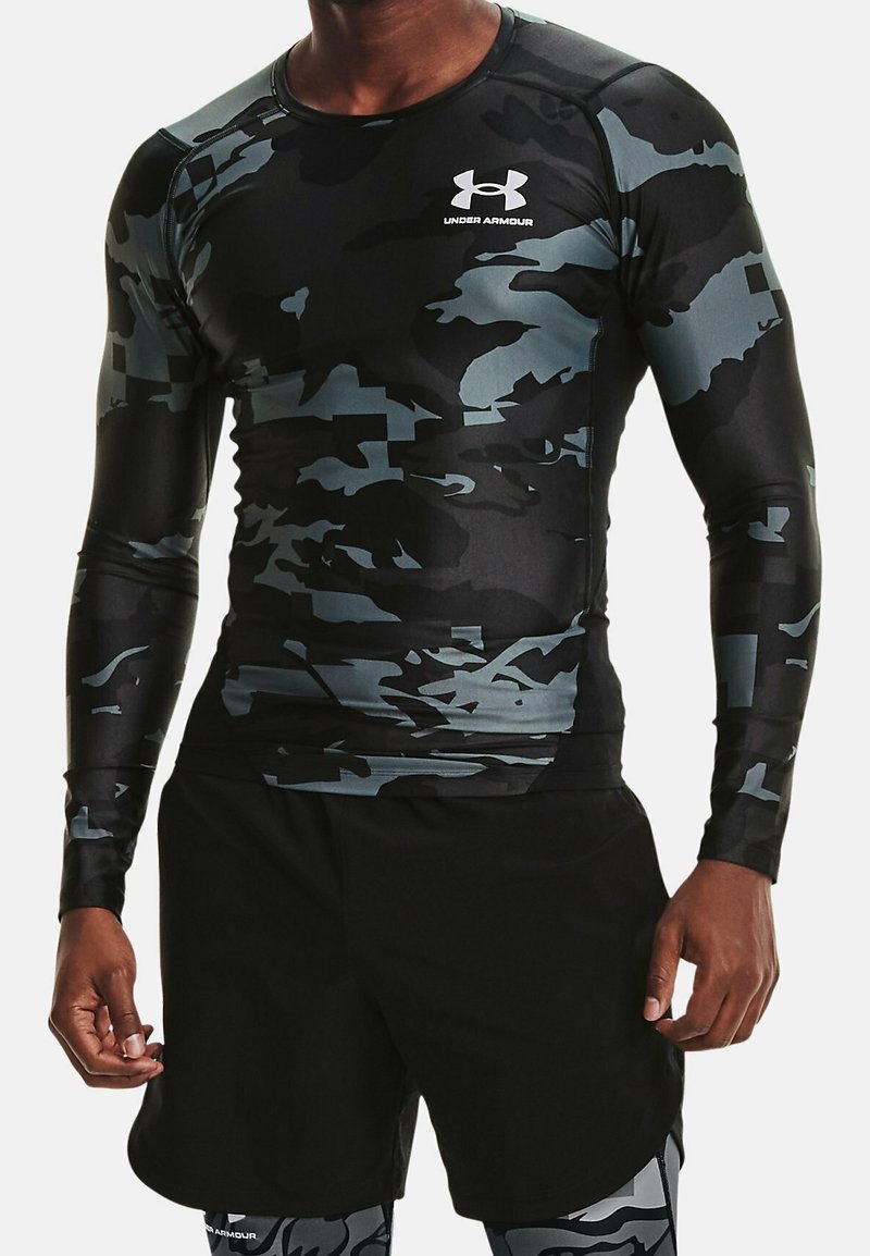 Atleet in zwart en grijs camouflage Under Armour langwerpig compressieshirt met zwarte shorts en bijpassende leggings.