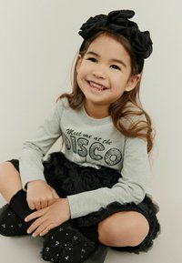 Sivá košeľa s dlhým rukávom a textom "Potkajte ma na DISCO", čierna riasená sukňa, čierne čižmy so zirkónmi a čierny textilný čelenka.