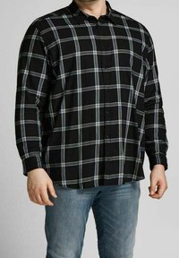 Camicia a maniche lunghe a quadri nera con un motivo a scacchi grigio e blu, abbottonata davanti e colletto aperto. Indossata con jeans azzurri chiari.