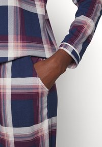 Katoenen plaid loungewear in de kleuren marineblauw, bordeaux en wit. De top heeft een ronde hals en de broek heeft zijzakken.