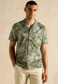 Krátky rukáv zelená košeľa s bielym tropickým vzorom, ktorý zobrazuje palmy a jachty. Obsahuje náprsné vrecko a zapínanie na gombíky.