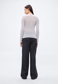 Svetlo siva rebrasta pletena majica z dolgimi rokavi, kombinirana z širokimi temnimi jeans hlačami, prikazana od zadaj na nevtralnem ozadju.