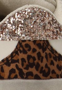 Zapato con parte superior de ante beige, acento brillante en oro rosa y un panel de impresión de leopardo marrón. Textura suave con detalles contrastantes.