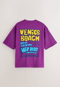 T-shirt violet à manches courtes avec un texte coloré ""Venice Beach Old Skool Hip Hop Carnival"" au dos en lettres jaunes et bleues.