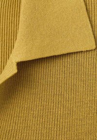 Tessuto lavorato a maglia in giallo senape, con motivo costine testurizzato e bordi lisci, che dimostrano flessibilità e morbidezza.