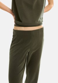 Olive-zielony top i pasujące spodnie wykonane z miękkiego materiału, charakteryzujące się luźnym krojem oraz gładką strukturą, z prostymi nogawkami i bocznymi szwami.