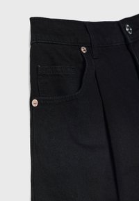 Pantalones de mezclilla negra con un bolsillo frontal, diseño plisado y acentos de hardware metálico en la cintura y el bolsillo.