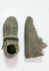 Zapatillas altas de gamuza verde con detalles perforados, cordones planos y una correa envolvente, que cuentan con una suela de goma texturizada.