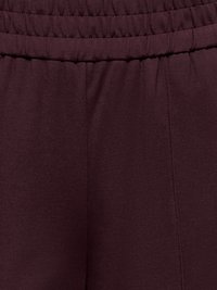 Gros plan sur une ceinture élastique de couleur bordeaux foncé avec des coutures verticales subtiles sur un pantalon en tissu doux.