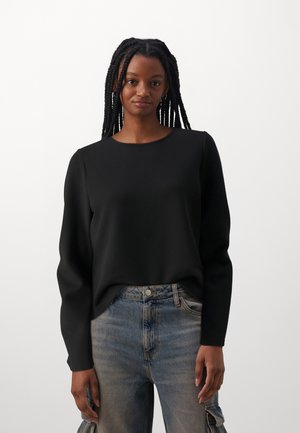 Svart langermet topp med rund hals, laget av glatt stoff; kombinert med lyseblå denimjeans med lomme detaljer.