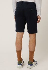 Navyblauwe shorts met twee achterzakken, lussen voor een riem en een strakke uitstraling. Gekocht met bruine sokken en multikleurige schoenen.