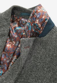 Grau mit Fischgratmuster versehene Jacke mit einer braunen blumigen Innenausstattung. Enthält einen einfarbigen blauen Kragenakzent und ein kleines rotes Nähdetail.