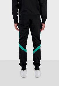 Černé sportovní kalhoty s modrozelenými diagonálními pruhy, elastickým pasem a manžetami, s úzkým střihem a měkkou texturou látky.