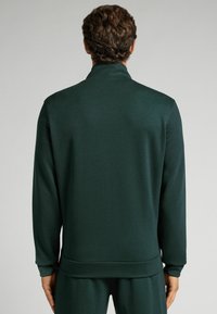 Sudadera de color verde oscuro con cuello alto y mangas largas. Textura suave, ajustada a la cintura con un dobladillo acanalado. Diseño general minimalista.