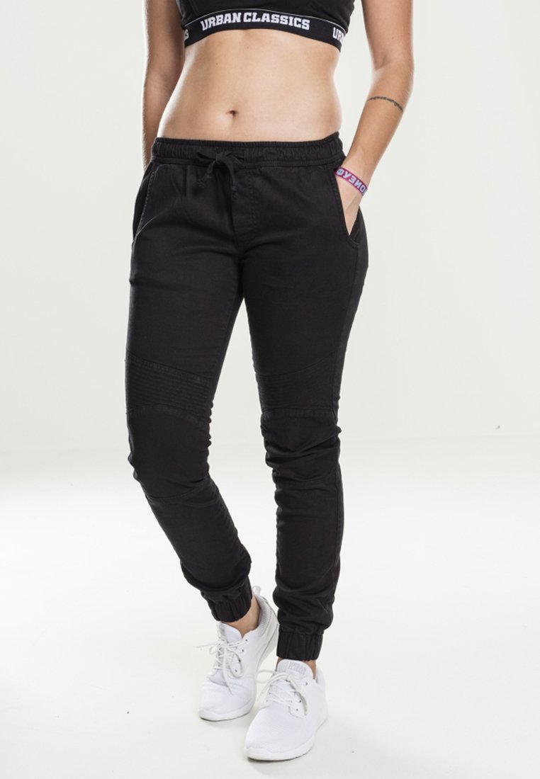 Svarta joggingsbyxor med framfickor, elastiska muddar och en slät textur. Bärs med en svart croppad topp och vita sneakers.