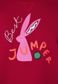 Jersey rojo con un gráfico de un conejo rosa sosteniendo una pelota verde y el texto "Mejor JERSEY" en letras naranjas y negras.