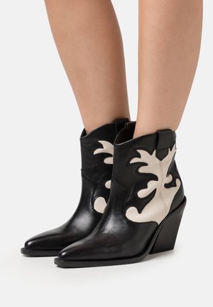 Leather ankle boots featuring a pointed toe, a black base with white flame-like appliqués, and a chunky heel for stability.