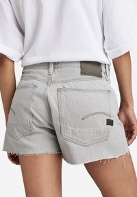 Harmaat farkkushortsit, joissa on rispaantuneet reunat, kaksi takataskua ja logotagg vyötärönauhassa. Yksinkertainen muotoilu, jossa on ompeluyksityiskohtia.