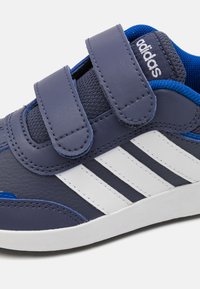 Baskets en cuir synthétique bleu avec deux bandes Velcro, rayures blanches sur le côté, languette en mesh texturé et semelle en caoutchouc.