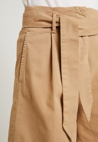 Beige high-waisted shorts met een brede stoffen riem, zijzakken en een gladde textuur, met strakke lijnen en een relaxte pasvorm.