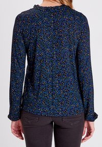 Hedvábná košile s dlouhým rukávem v tmavě modré barvě se vzorem listů, s nabíranými detaily u krku a hladkou texturou látky.