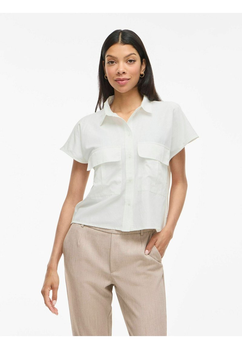 Lichtgekleurde shirt met korte mouwen en kraag, voorzien van twee borstzakken, knoopsluiting en een relaxed fit. Gepaard met beige broek.